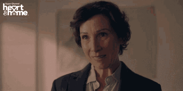 a woman in a suit is smiling in front of a sign that says heart & home