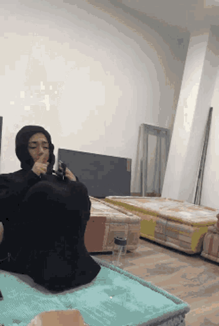 a person wearing a black hoodie sits on a bed in a room