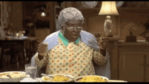 an elderly woman sitting at a table with plates of food and a lamp