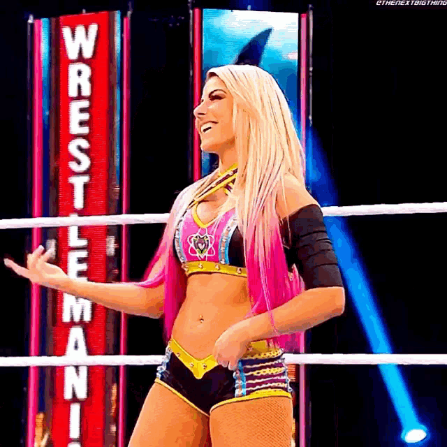 a woman is standing in a wrestling ring wearing a pink top and shorts .
