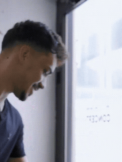 a man in a blue shirt is standing in front of a window .