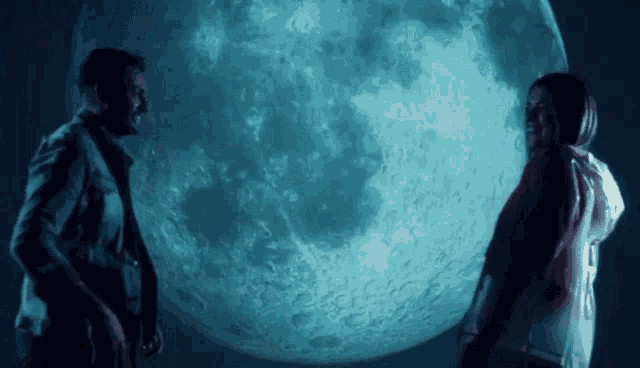 a man and woman stand in front of a full moon