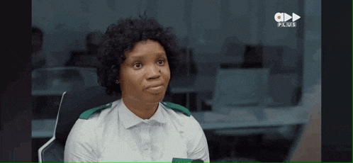 a woman in a white shirt with green trim is sitting in a chair and making a face .