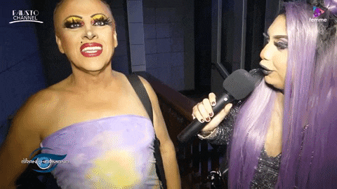 a woman with purple hair is holding a microphone and talking to a man with makeup on
