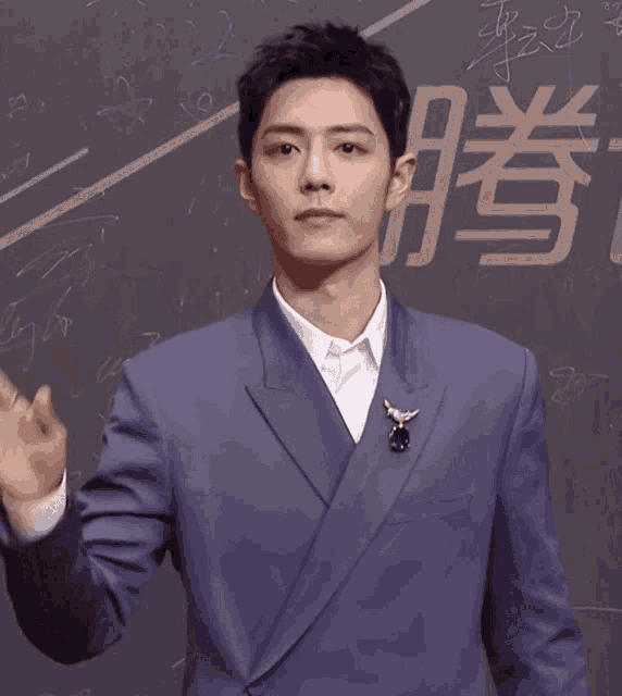 a man in a purple suit is waving his hand in front of chinese writing