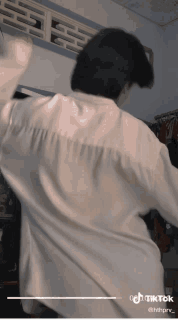 a man in a white shirt is dancing in a room with clothes hanging on the wall behind him