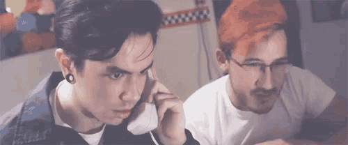 a man with red hair is talking on a cell phone next to another man with glasses .