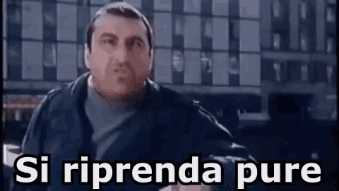 a man in a black jacket is standing in front of a building with the words `` si riprende pure '' written on it .