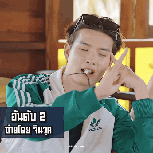 a man wearing a green and white adidas jacket is making a funny face