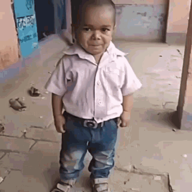 a little boy wearing a white shirt and blue jeans is standing on a sidewalk with his hands in his pockets .