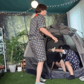 a man is standing in front of a tent in a room with two other people sitting in it .