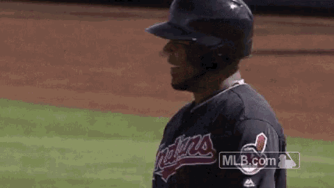 a baseball player wearing a helmet and a cleveland indians jersey is standing on the field .