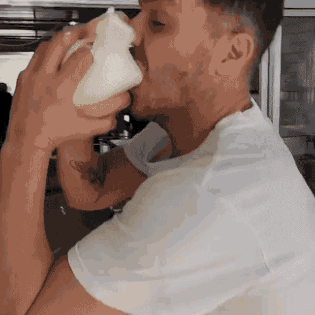 a man in a white shirt is drinking from a cup .