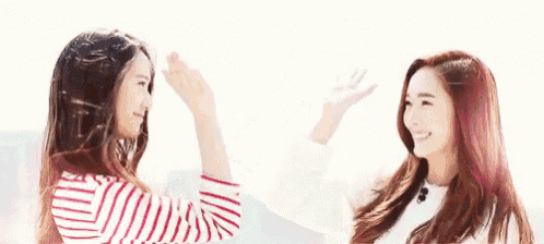 two young women are giving each other a high five while standing next to each other .