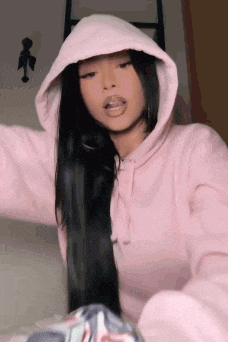 a woman is wearing a pink hoodie with her tongue out .