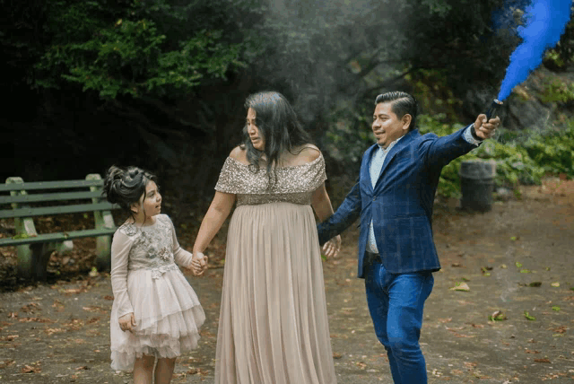 a man in a suit holds a blue smoke bomb while walking with a woman and a little girl