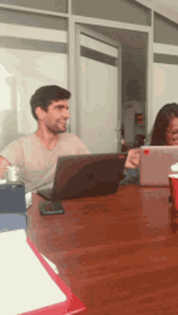 a man is sitting at a table with a laptop and a woman is sitting at a table with a tablet