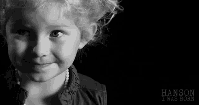 a black and white photo of a little girl with a pearl necklace .