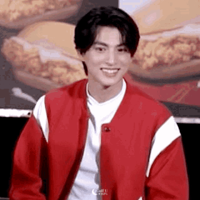 a young man in a red jacket is smiling in front of a burger .