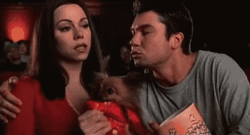 a man is kissing a woman on the cheek while holding a box of popcorn .