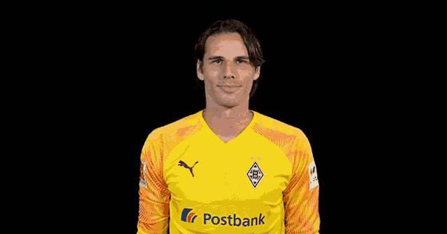a soccer player wearing a yellow postbank jersey gives a thumbs up