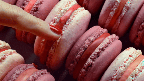 a close up of a person 's finger on a row of pink macarons