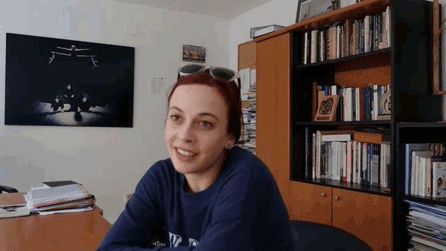 a woman wearing sunglasses and a blue sweatshirt with the word ny on it sits at a desk