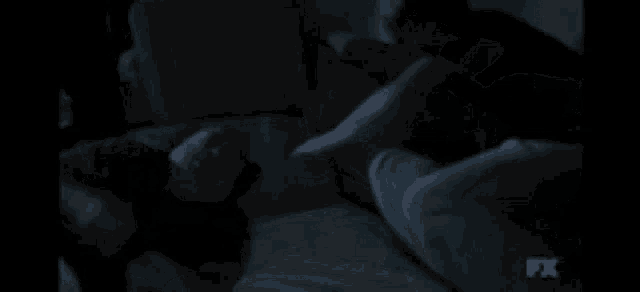 a person is laying on a bed in a dark room with a fx logo in the background .