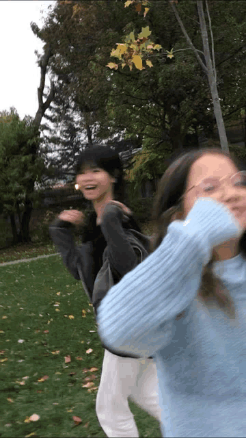 a girl in a blue sweater is standing next to another girl in white pants