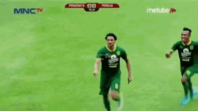 two soccer players are celebrating a goal on a field with mnctv in the background
