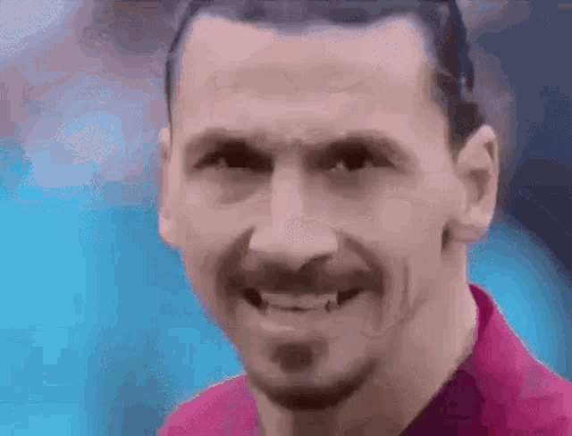 a man with a beard wearing a pink shirt smiles for the camera