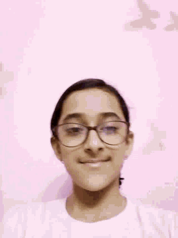 a woman wearing glasses is smiling in front of a pink wall with butterflies