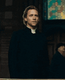 a priest standing in front of a stained glass window in a church .