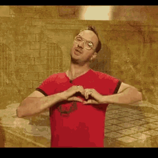 a man wearing glasses and a red shirt is making a heart with his hands .