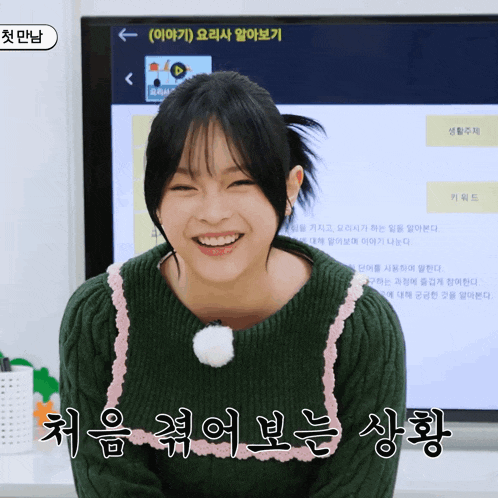 a girl in a green sweater is smiling in front of a screen that says ' a ' on it