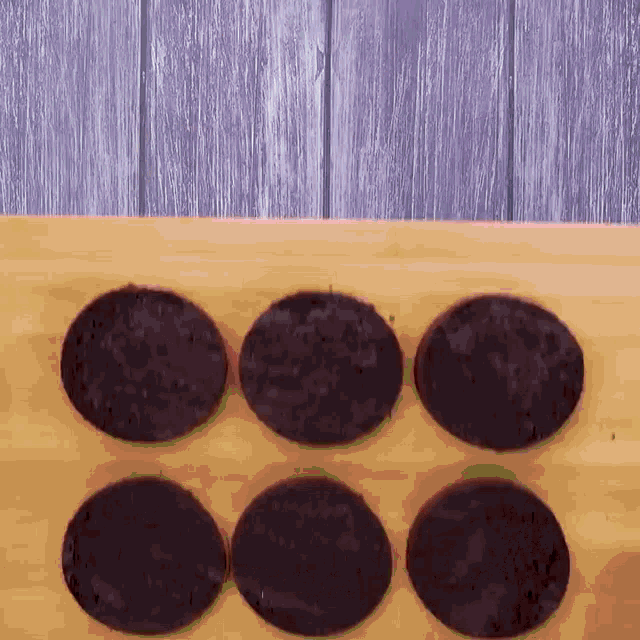 six chocolate cookies are sitting on a wooden surface