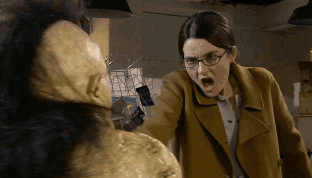 a woman wearing glasses and a brown coat screams at a monster