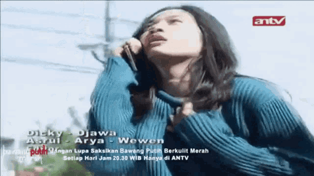 a woman in a blue sweater is talking on a cell phone .