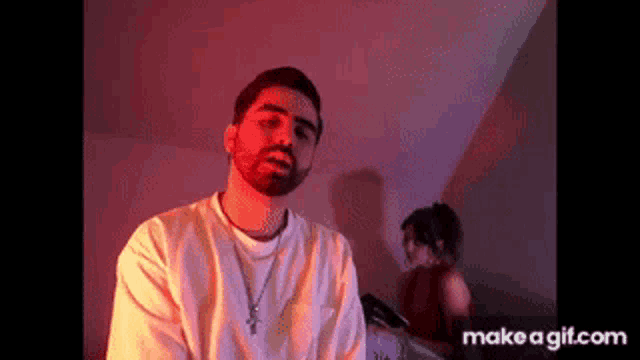 a man with a beard and a cross necklace is standing in front of a woman in a red dress .