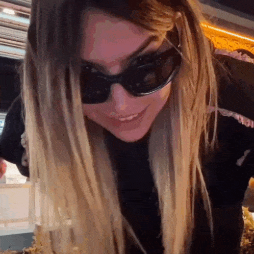 a woman wearing sunglasses is smiling and looking down