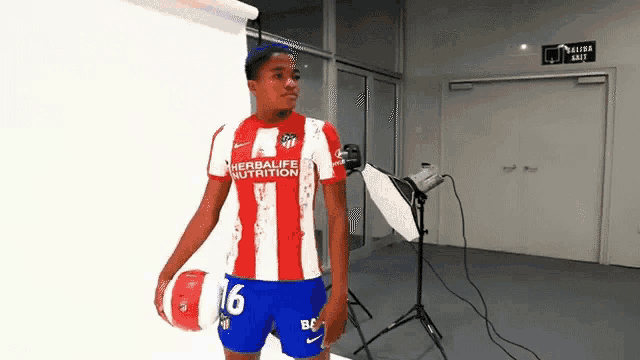 a man in a red and white striped shirt and blue shorts is holding a soccer ball in a room .