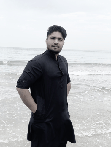 a man in a black shirt is standing on a beach with his hands in his pockets