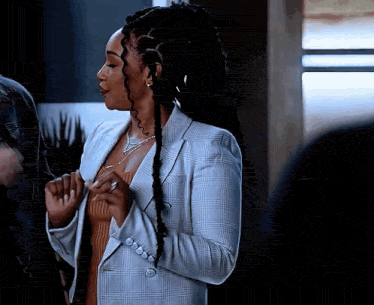 a woman with dreadlocks is wearing a plaid jacket and a sweater .