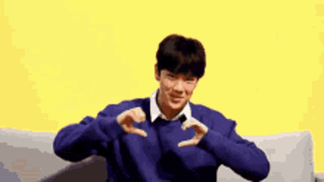 a man in a blue sweater is making a heart with his hands