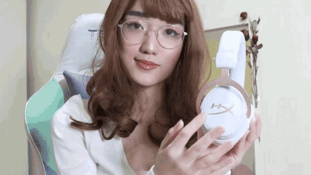 a woman wearing glasses is holding up a pair of hyperx headphones
