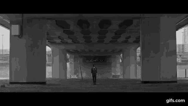 a black and white photo of a man walking under a bridge .