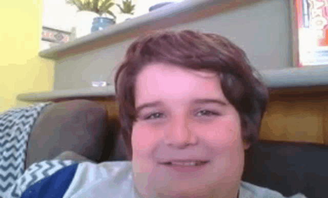 a young boy is sitting on a couch smiling at the camera .