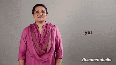 a woman in a pink shirt and scarf is giving a yes sign .