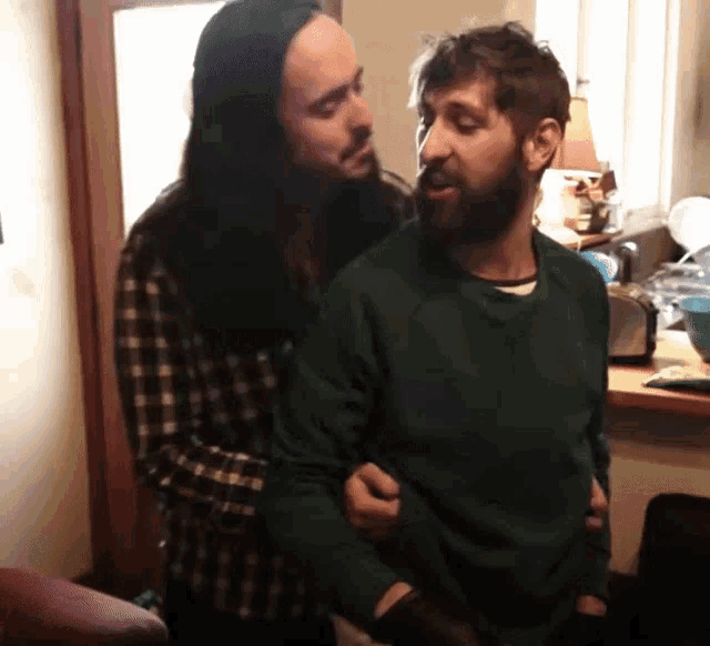 a man with long hair and a beard is holding another man 's arm