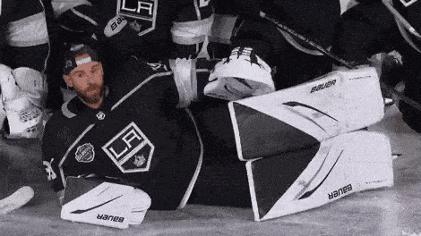 a hockey goalie is laying on the ice with his legs crossed and his pads on .